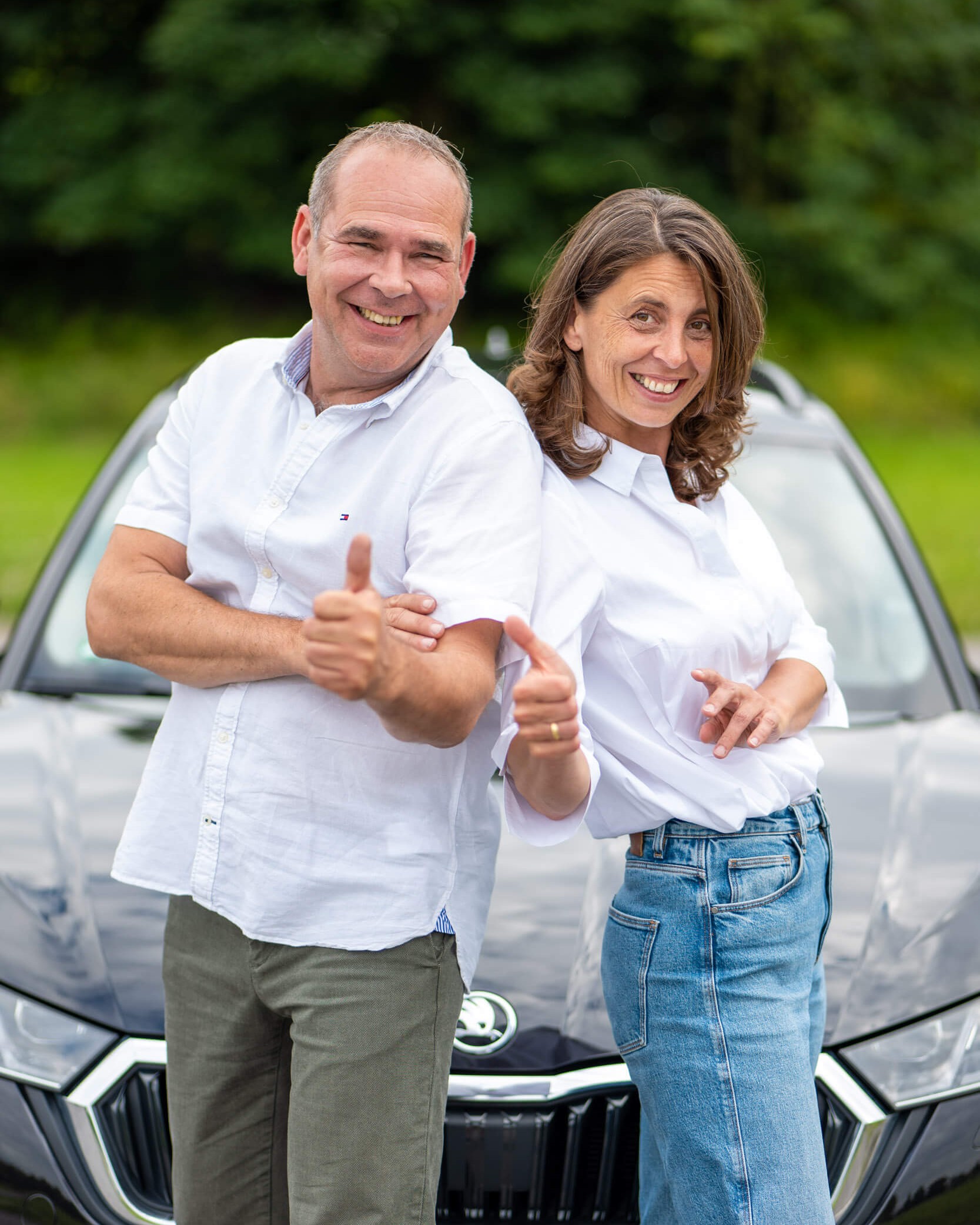 Ein fröhliches Paar posiert lässig vor einem schwarzen Auto im Freien.