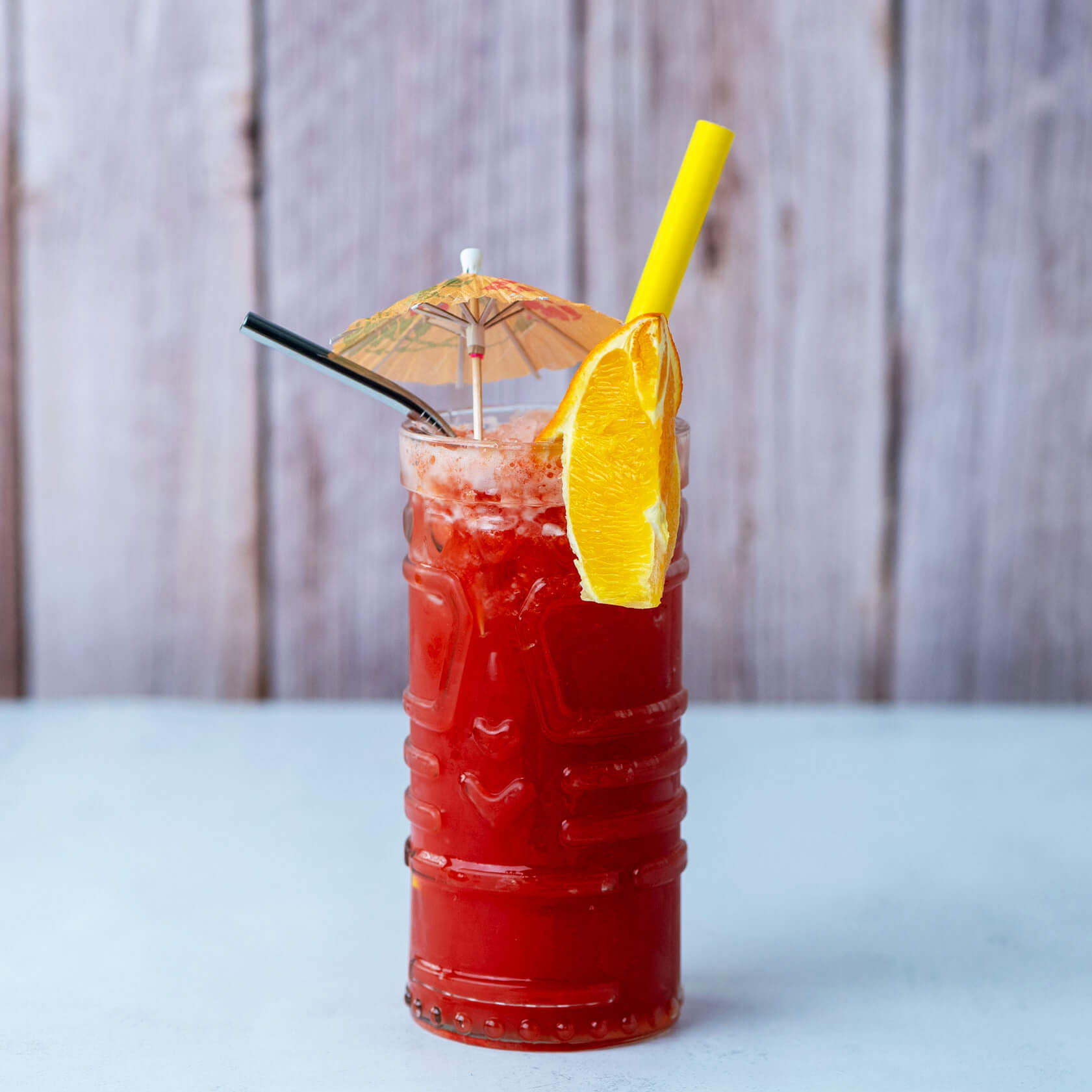 Erfrischender Cocktail mit fruchtigem Mix, dekoriert mit Schirmchen und Orangenscheibe.