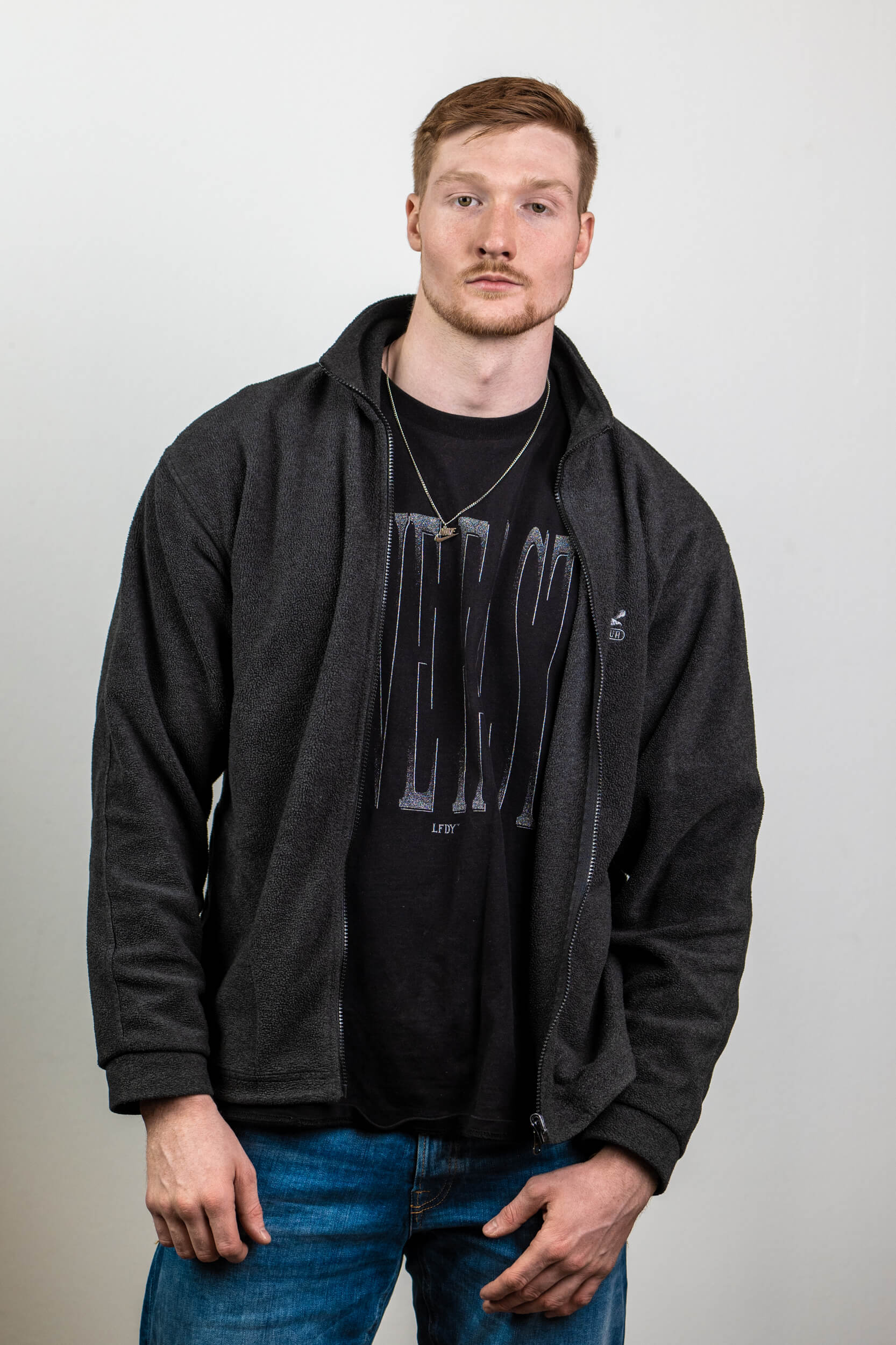 Junger Mann in grauem Sweatshirt und schwarzem T-Shirt. Neutrale Hintergrundfarbe.