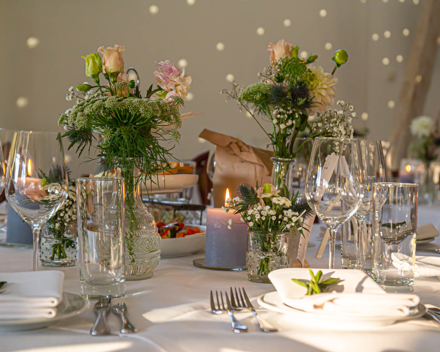 Elegant gedeckter Tisch mit Blumen, Kerzen und gläsernem Geschirr in warmer Atmosphäre.