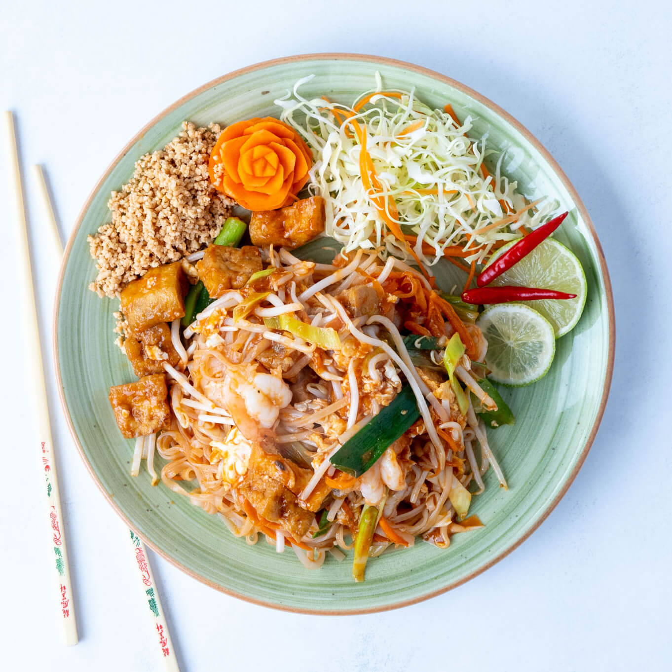 Bunter Teller mit Pad Thai, Garnelen, Gemüse, Erdnüssen und frischen Beilagen.