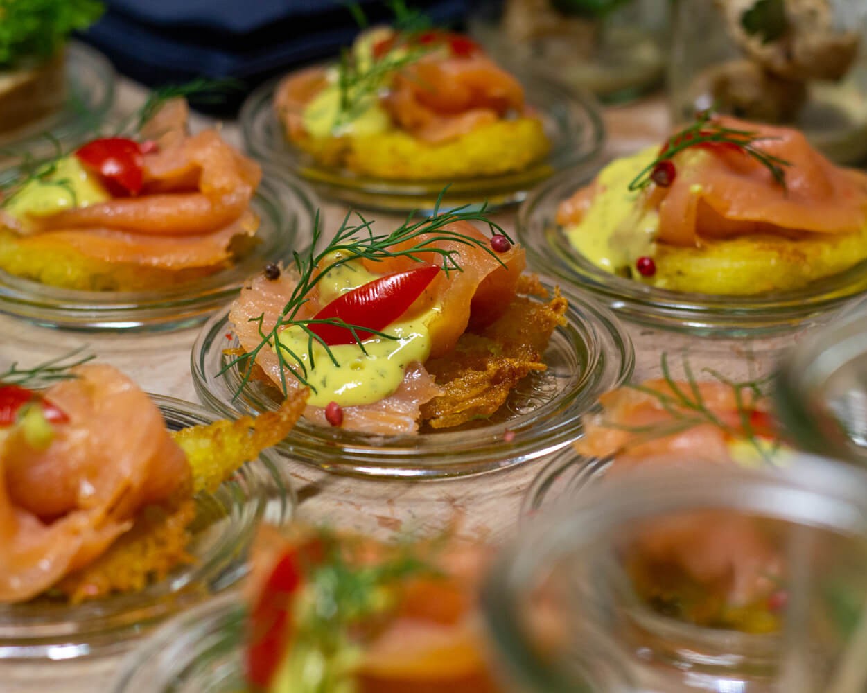 Gourmet-Häppchen mit Räucherlachs, Sauce und Deko in kleinen Gläsern arrangiert.