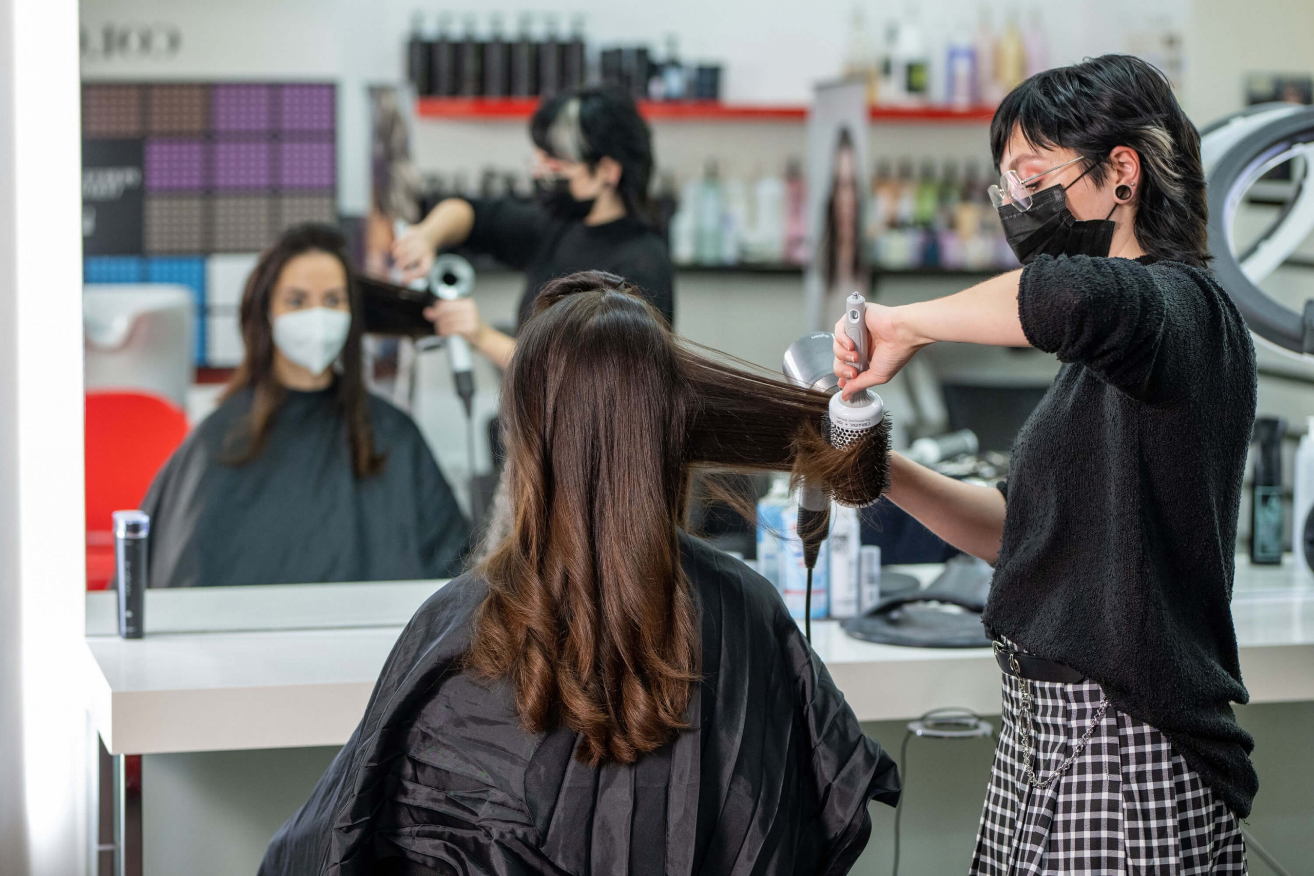 Friseursalon mit Kundin, die frisiert wird, während eine Stylistin Haare glättet.