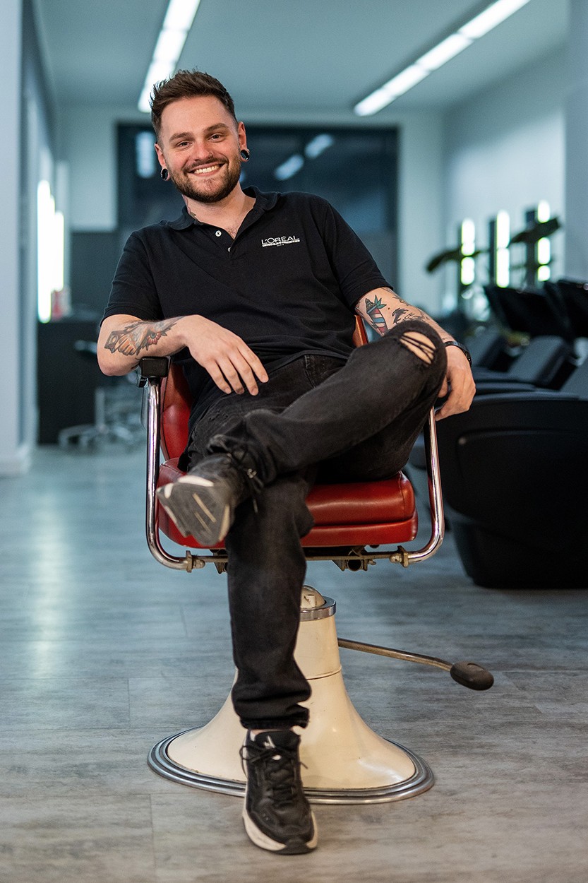 Frisör sitzt entspannt in einem roten Stuhl in einem modernen Salon.