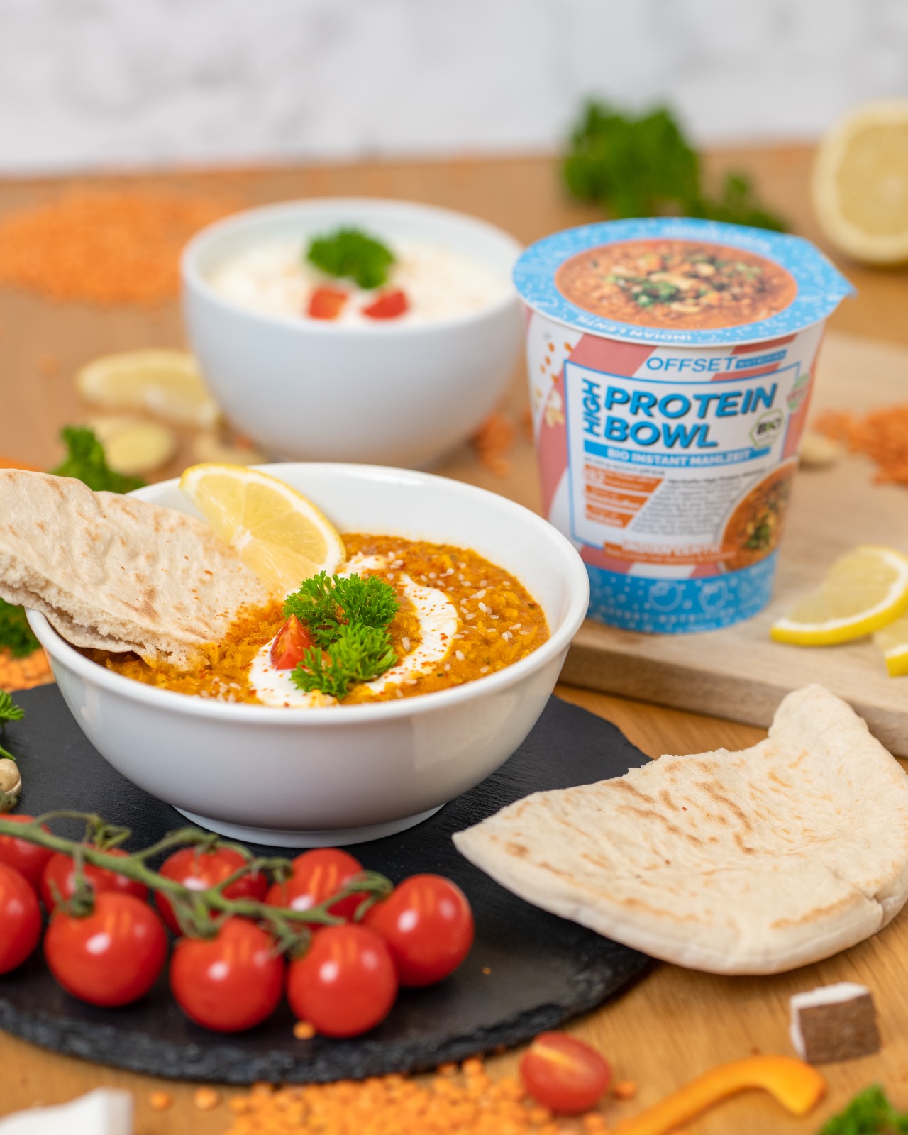 Bunte Mahlzeit mit Linsensuppe, frischen Tomaten und Fladenbrot auf Holzoberfläche.