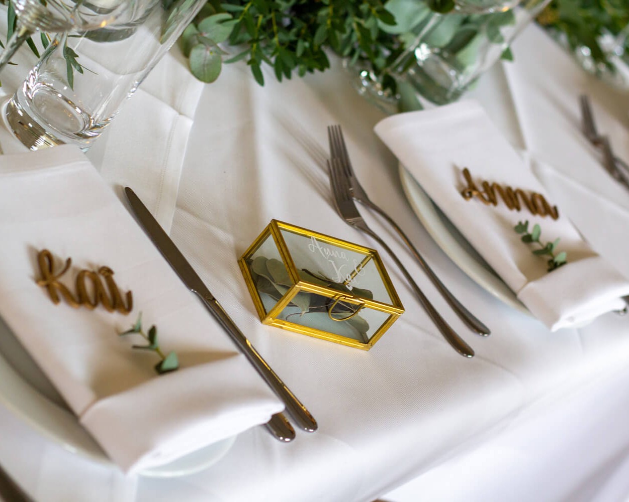 Elegant gedeckter Tisch mit personalisierten Servietten und einem dekorativen Glaskasten.