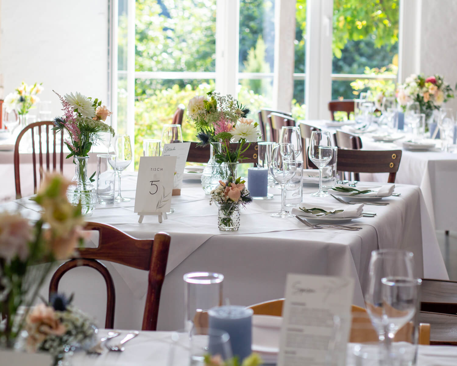 Elegant dekorierter Tisch mit Blumen, Gläsern und Menükarte in hellem Raum.