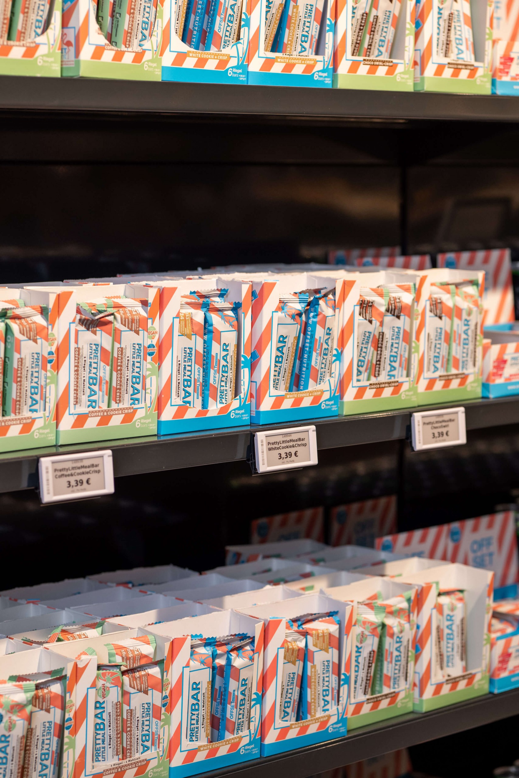 Regal mit verschiedenen Packungen von Snack-Riegeln, deutlich mit Preisen ausgezeichnet.