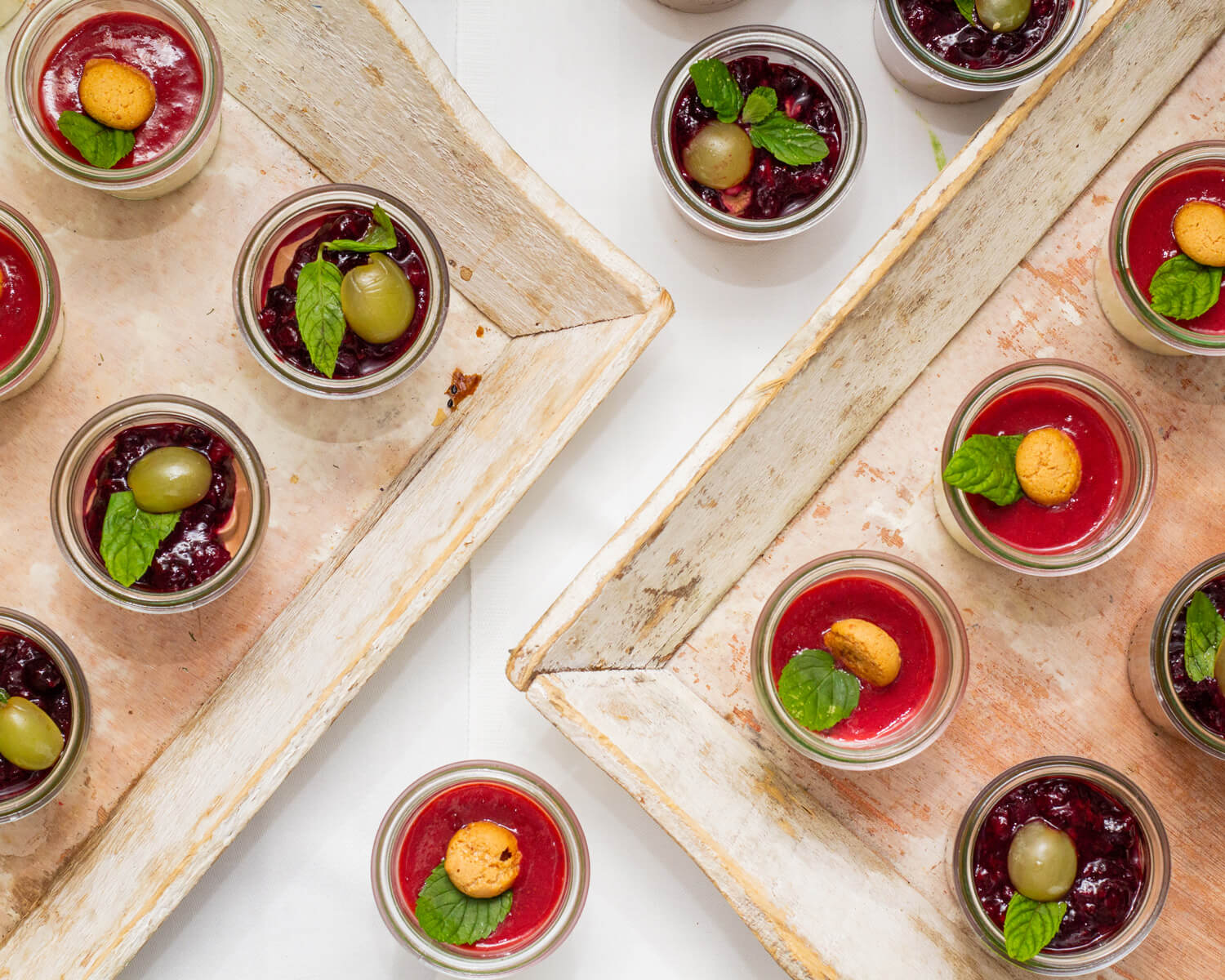 Zwei Tabletts mit verschiedenen Desserts in Gläsern, garniert mit Früchten und Minze.