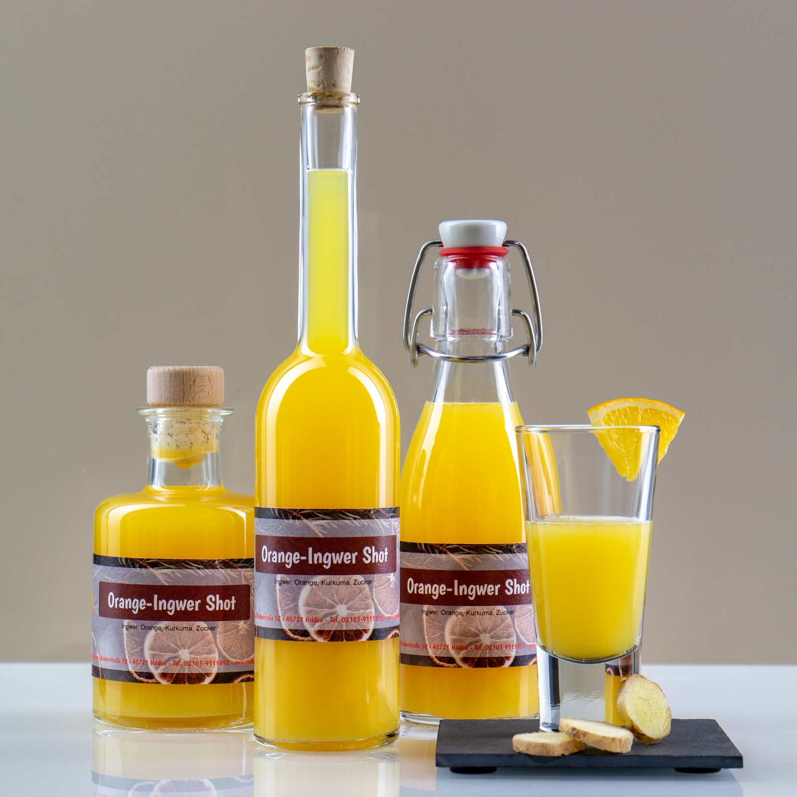 Drei Flaschen und ein Glas mit leuchtend gelbem Orange-Ingwer-Shot und einer Orangenscheibe.