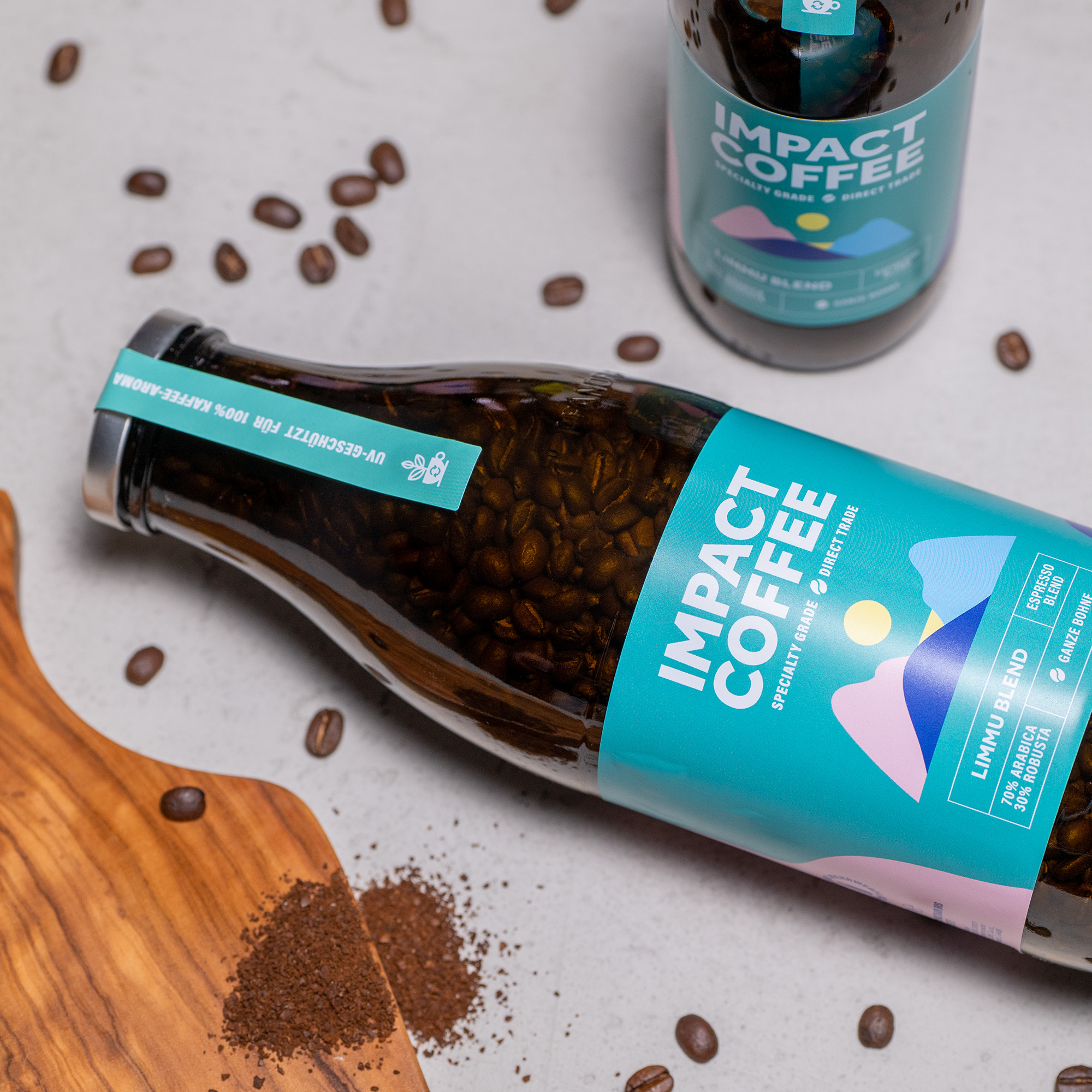 Flasche mit Impact Coffee, gefüllt mit Kaffeebohnen, neben gemahlenem Kaffee und Holzunterlage.